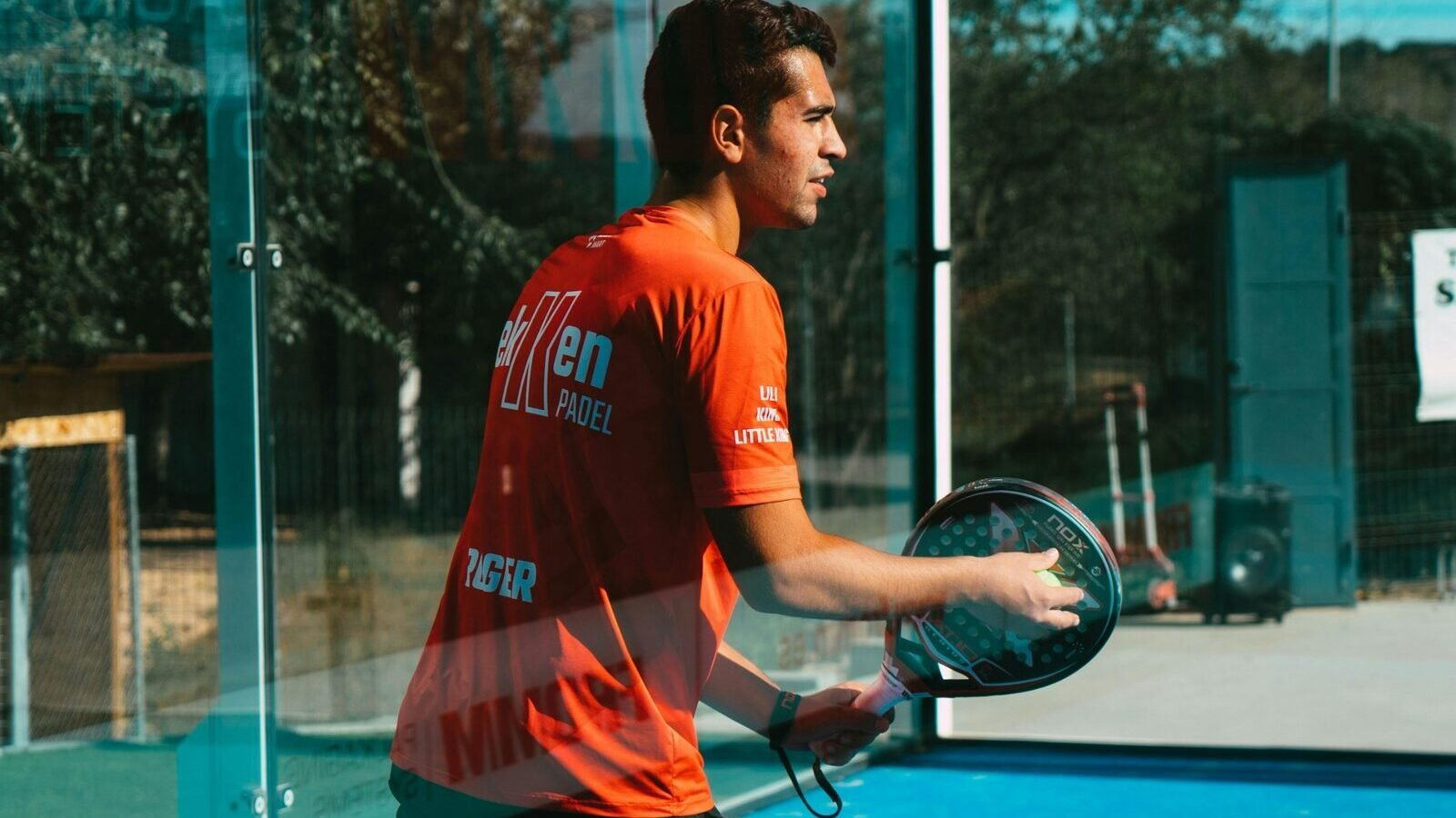 Joueur de padel avec sa raquette près d’une vitre