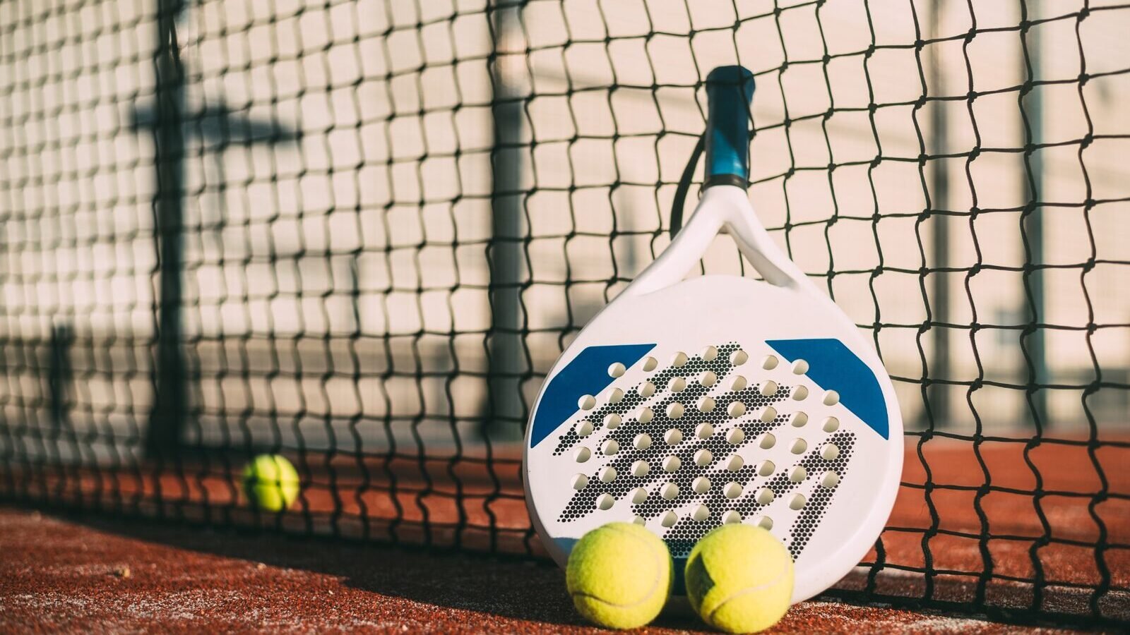 Raquette et balles de padel posées contre un filet