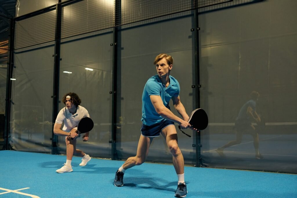 Deux joueurs se déplacent devant les vitres d’une piste de padel